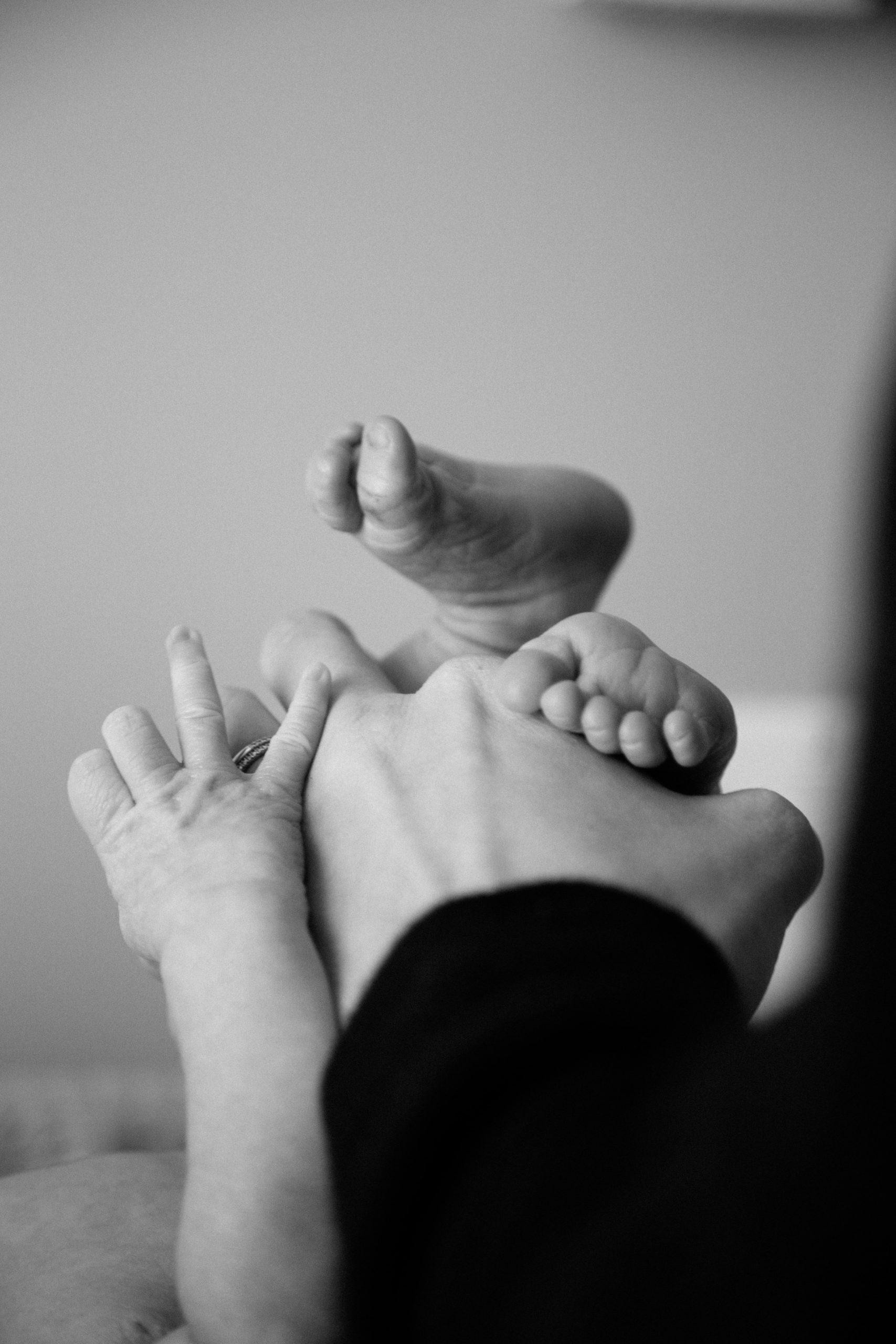 A black and white image of a baby's feet and an adult hand. This photo illustrates the challenges parents experience after bringing a child home. These parents can seek support from postpartum therapy in Los Angeles, CA. | 91006 | 90071