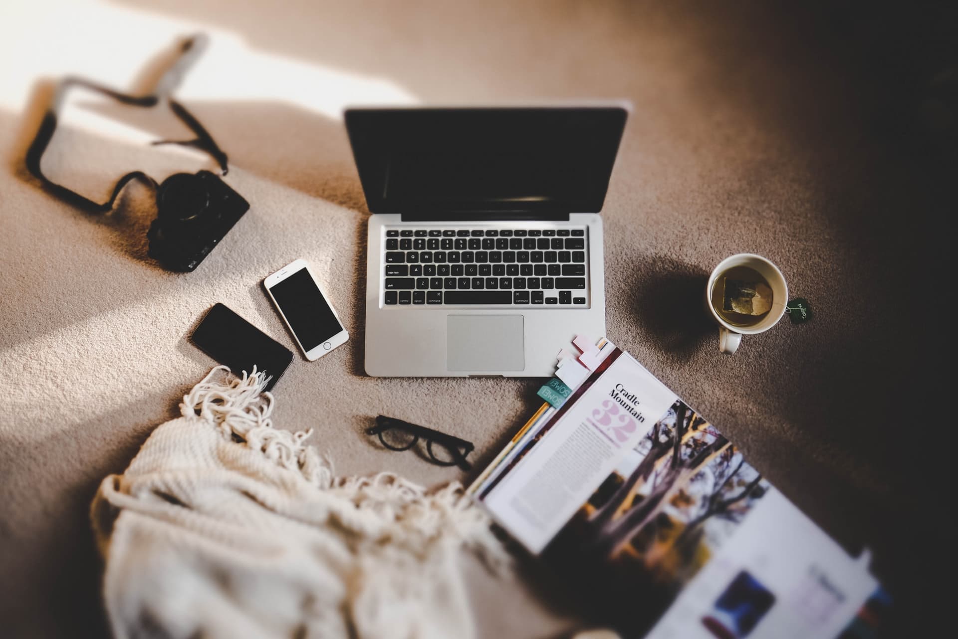 Image of a laptop, phone, glasses, camera, book, and tea sitting on the floor. This image illustrates what your work-life balance looks like before starting burnout treatment and work stress management in Los Angeles, CA. 91006 | 90071