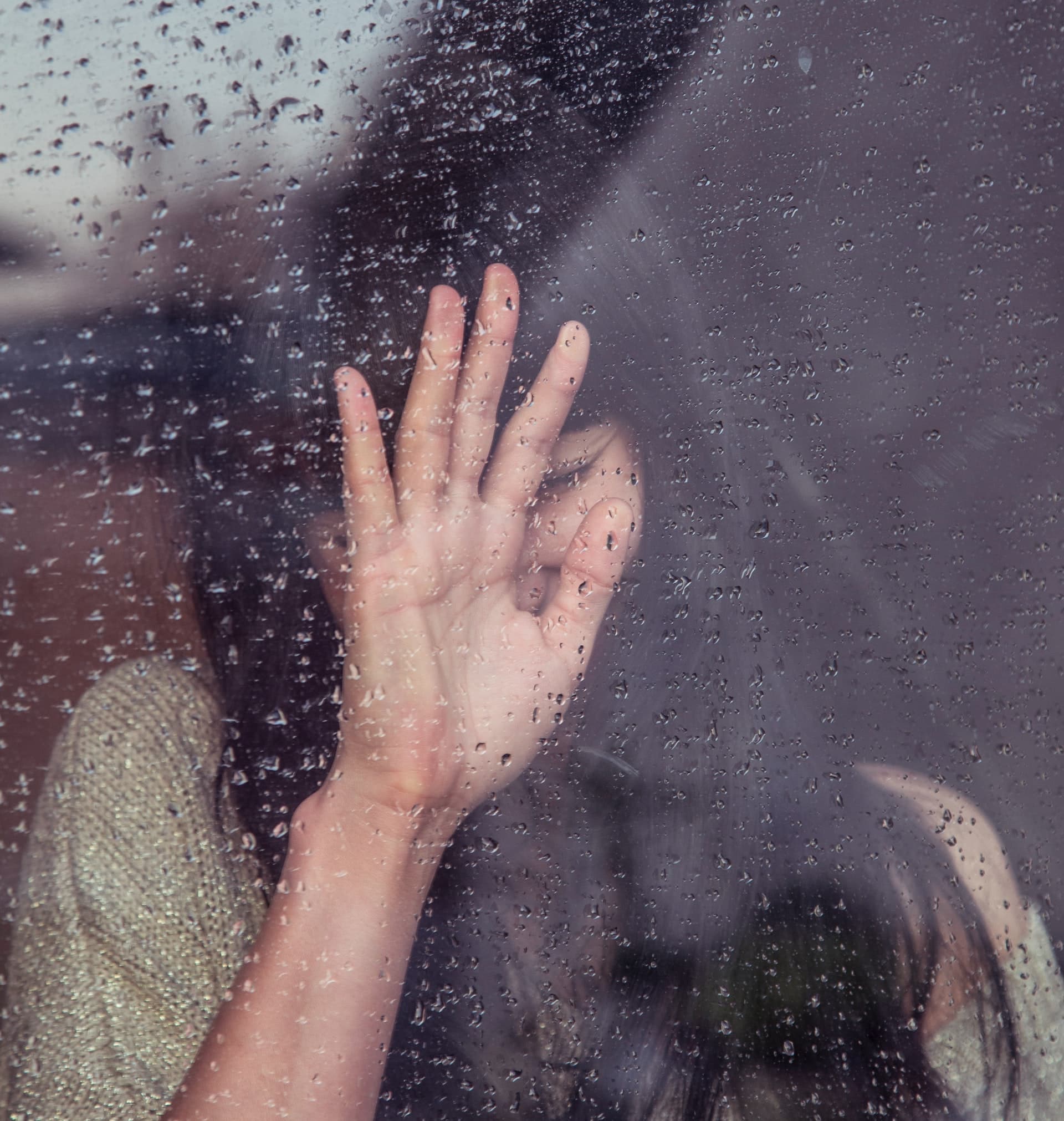 Photo of a young Asian woman with her hand against a window with raindrops on it. This photo represents how many people feel before working with an Asian therapist for anxiety treatment in Los Angeles, CA. 90071 | 90232