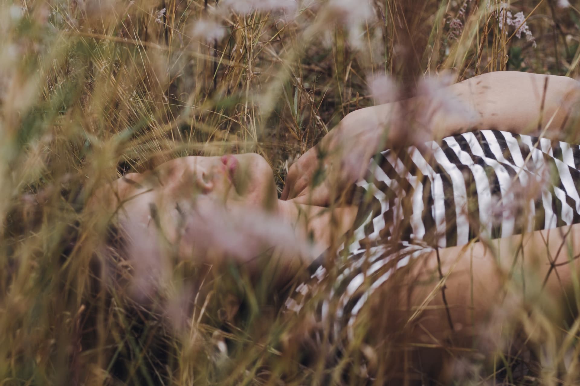 Image of a young Asian woman laying in a field with her hand on her chest. She appears to represent a person having a panic attack and is going to look for anxiety treatment in Los Angeles, CA this week. 91108 | 91006