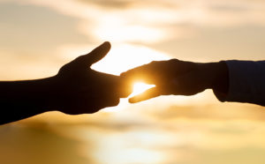 Image of two hands touching with a yellow sunset in the background. This image illustrates how working with a trauma therapist in Los Angeles, CA can help you heal from racial trauma. | 90404 | 90503