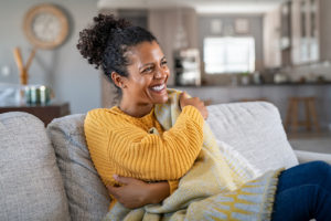 Image of a woman wearing a yellow sweater sitting on a couch and smiling. This image represents the support that women in a postpartum support group in Los Angeles, CA can receive when meeting with other parents. | 91006 | 90071