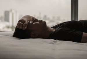 Image of an Asian man laying down and holding his arm to his forehead in exhaustion. This image illustrates the numbness that those with racial trauma may experience before starting trauma therapy in Los Angeles, CA with a trauma therapist. | 90504 | 90505
