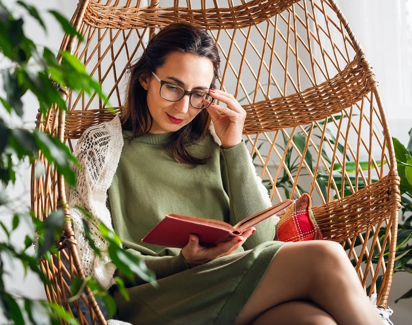 Image of a woman sitting in a woven chair reading a book. This image depicts someone who might benefit from adult ADHD treatment in Los Angeles, CA. Reach out to get started with an adult ADHD therapist today. | 91108 | 90232
