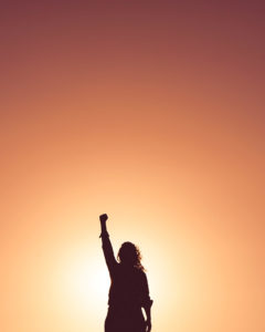 Image of person holding their fist in the air against an orange background. This image could depict someone who is just getting started with teen therapy in Los Angeles, CA. Online therapy for teens in California allows you to meet with a teen therapist from afar. | 91108 | 90232