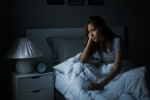 Image of a woman sitting in bed looking frustrated. This image illustrates the struggles in Asian American mental health one may face before meeting with a PTSD therapist in Los Angeles, CA. Trauma therapy and PTSD treatment can help. | 90504 | 90505