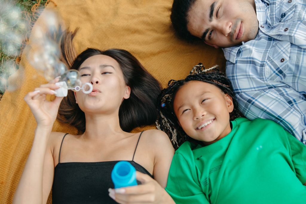 Image of three happy Asian youth lying on a blanket and blowing bubbles. This photo illustrates the happiness of kids, teens, and young adults who may find support in working with Asian Asian therapists in Los Angeles, CA. | 91108 | 90232