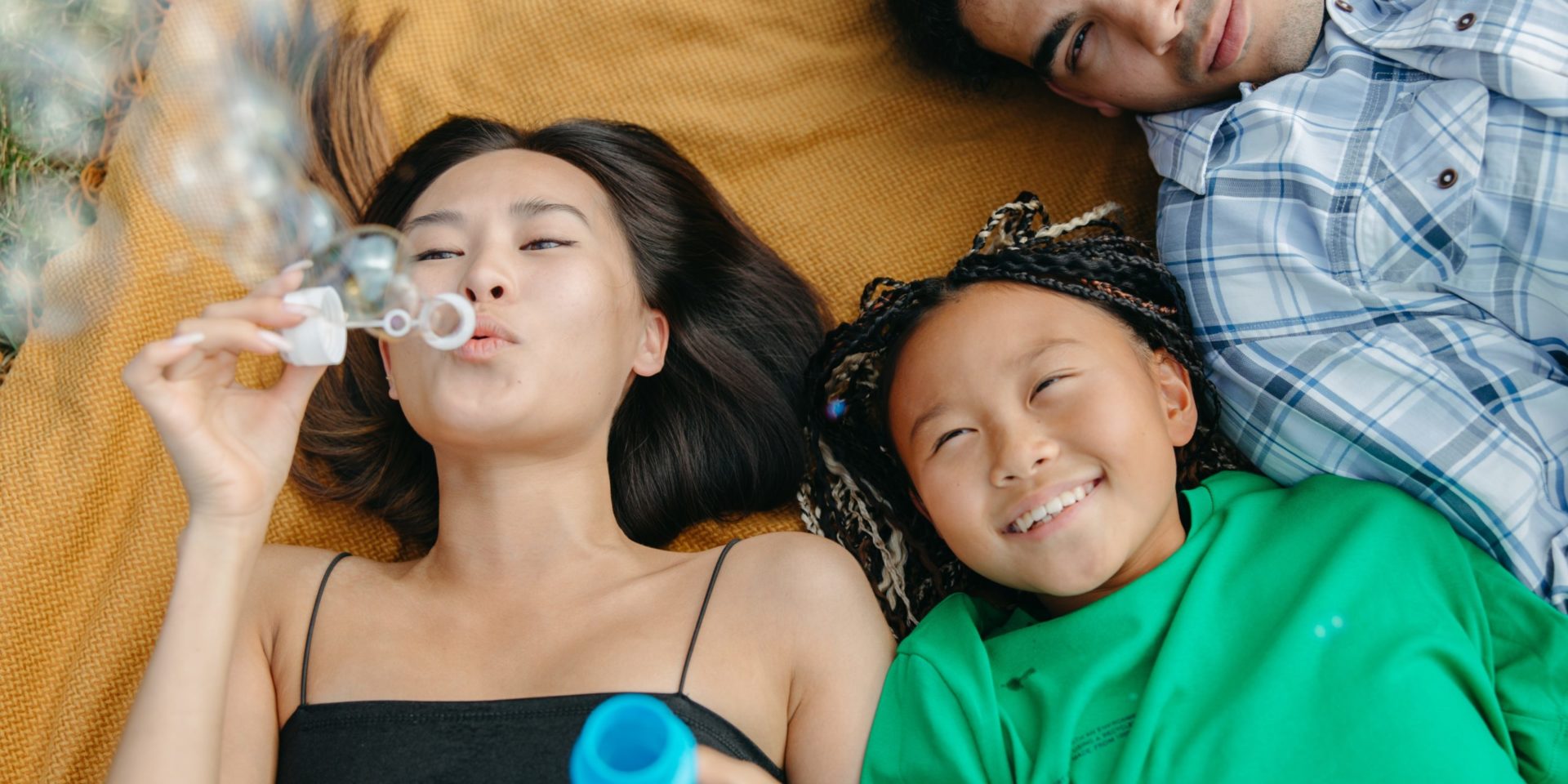 Image of three Asian family members blowing bubbles together. This photo illustrates the happiness found after working with an Asian therapist in Los Angeles, CA to work through family roles and obligations. | 91108 | 90232