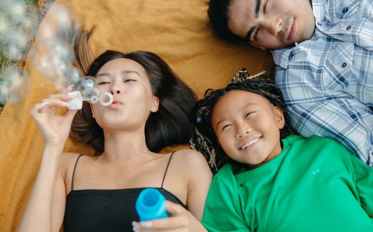 Image of three happy Asian youth lying on a blanket and blowing bubbles. This photo illustrates the happiness of kids, teens, and young adults who may find support in working with Asian Asian therapists in Los Angeles, CA. | 91108 | 90232