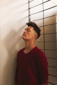 Image of a man wearing a red sweater with his eyes closed. This image could depict someone who could get support from an Asian therapist in Los Angeles, CA. Reach out for Asian American therapy today. | 91006 | 90071