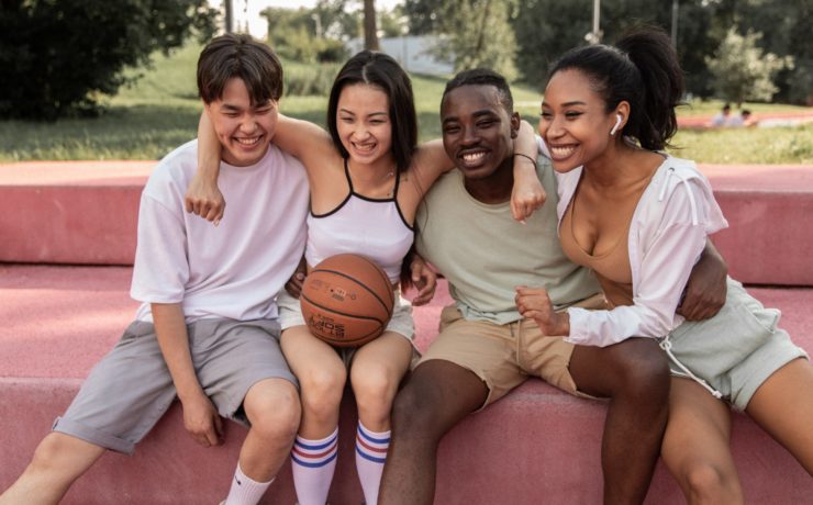 Happy multiracial teenagers with their friends embracing on bench after basketball training representing how Yellow Chair Collective can provide excellent Asian American teen therapy for Asian and Asian American teens in Southern California.