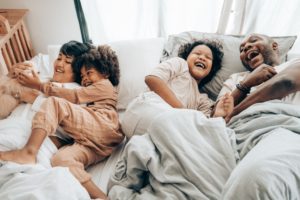 Interracial family laughing in a bed together representing how closer bonds can be formed with appropriate boundaries are established in the Los Angeles, California area.
