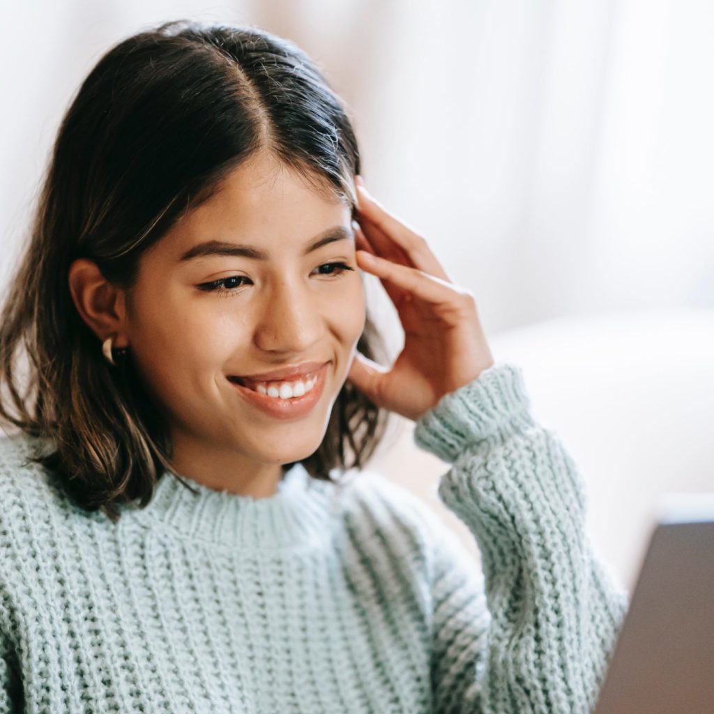 A woman smiling while working on her laptop representing the how effected online therapy with Yellow Chair Collective therapists can be in New York.