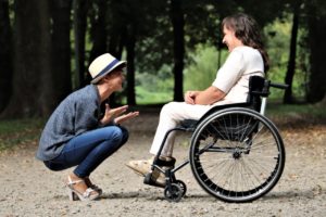 A woman who is a caregiver laughing with another woman who is in a wheelchair she is caregiving for to represent how people can find joy even in the midst of hard situations by getting therapy from a Yellow Chair Collective California or New York therapist.