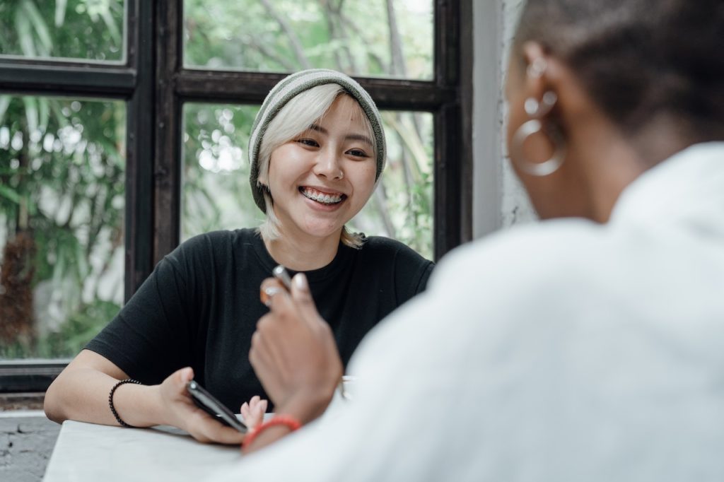 Photo of an Asian American woman smiling and talking to someone else. This photo represents how important it is to destigmatize mental health in New York so that other Asian Americans can find therapists to help them with their struggles. Learn more with Asian American Therapy in New York.