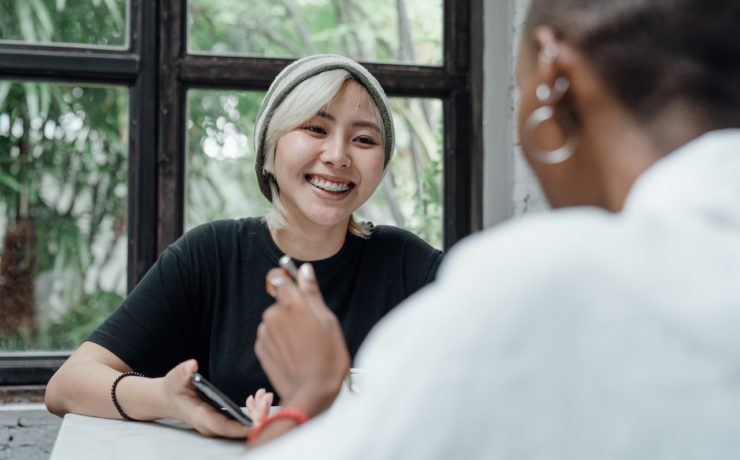Photo of an Asian American woman smiling and talking to someone else. This photo represents how important it is to destigmatize mental health in New York so that other Asian Americans can find therapists to help them with their struggles. Learn more with Asian American Therapy in New York.