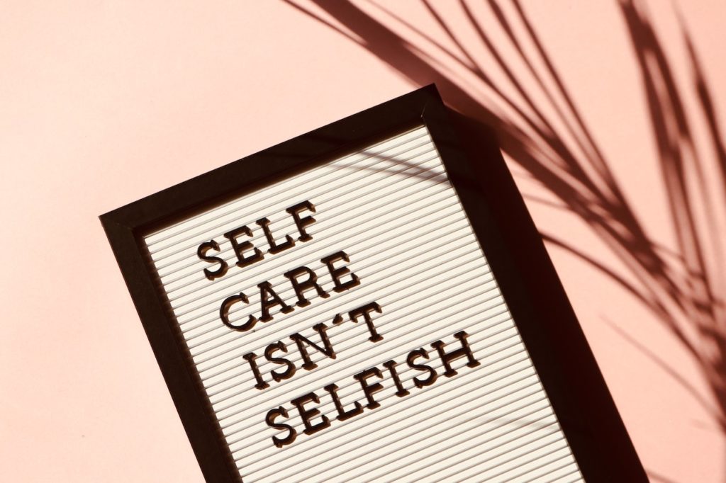 A photo of a sign that reads "Self Care Isn't Selfish" represents the valid stress and burnout caregivers can feel showing why therapy for caregivers in Los Angeles or New York City can be helpful to not feel alone and gain support.