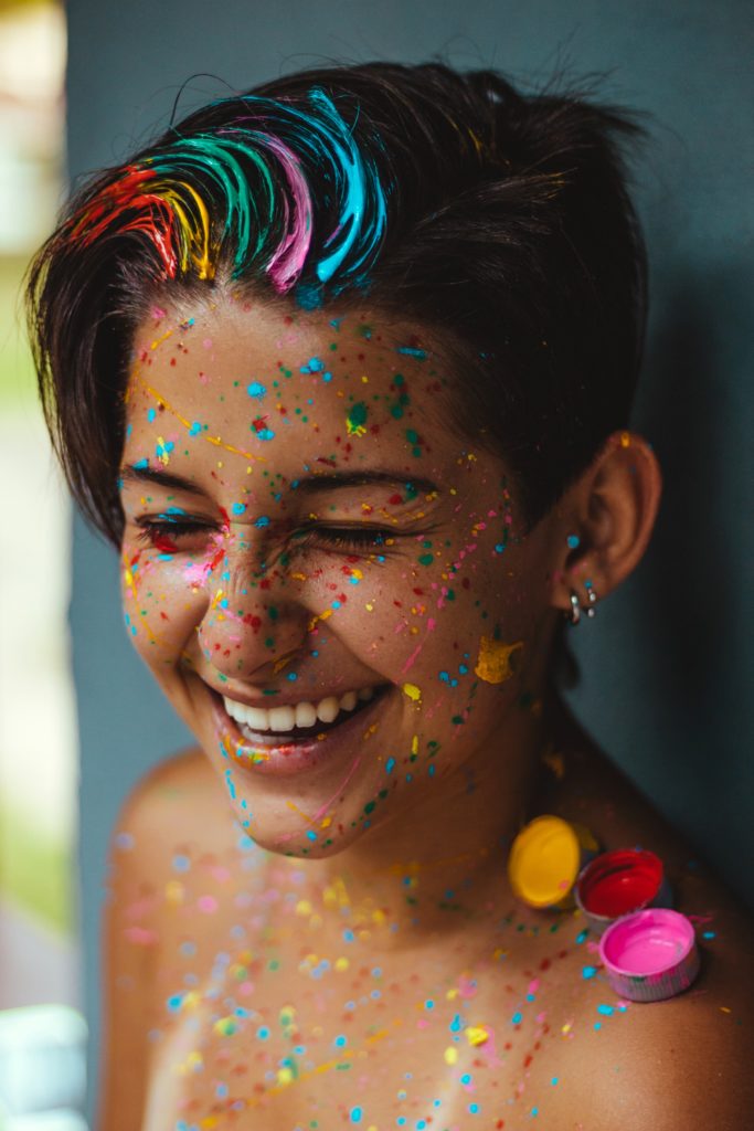 Photo of a girl smiling with multicolored paint splatters covering her face and in her hair. Discover how culturally sensitive therapy in Los Angeles, CA can help you heal your cultural wounds.
