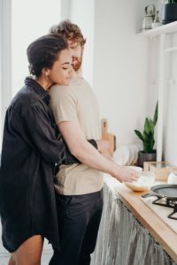 A Black woman and a white male hugging in a kitchen representing that a relationship can involve differing relationship styles in Los Angeles, California.