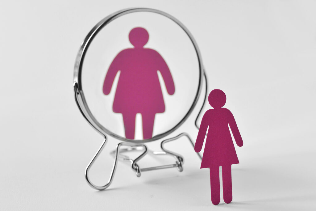 A paper cutout of a woman seeing a distorted reflection in a mirror. This could represent the distorted view and eating disorder support group in New York, NY can offer support with overcoming. Learn more about online therapy for asian americans by searching “asian american therapy in new york” today.
