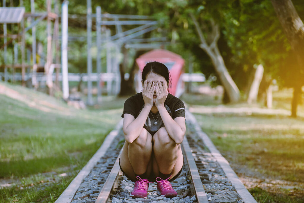 A woman covers her face while crouching on train tracks. This could represent the pain felt from collective trauma a trauma therapist in Los Angeles, CA can address. Learn more about trauma therapy in Los Angeles, CA, and more by contacting a stress management therapist in Los Angeles, CA.
