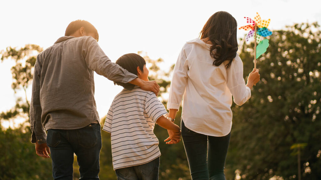 A family walks with their child on a sunny day. This could represent the closer bonds cultivated after trauma therapy in Los Angeles, CA. Learn more about overcoming collective trauma and the support a stress management therapist in Los Angeles, CA can offer today. 
