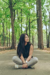 A woman sits on a forest trail while smiling. This could represent a grounding technique that therapy for Asian women in Los Angeles, CA can help cultivate. Learn more about the support therapy for asian women by contacting an Asian therapist in New York today.
