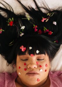 AA woman rests with flower petals on her face and hair. Learn how online therapy for asian americans can offer support with an Asian American therapist in Los Angeles by searching for an Asian American therapist near me today.
