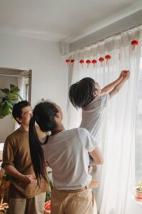A family of three hangs decorations on a window. This could represent the stronger bonds cultivated by working with an Asian American therapist. Learn more about online couples therapy in California and how an online therapist in los angeles, ca can help.
