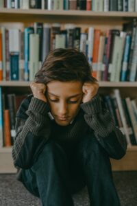 A child sits against a library shelf while covering their ears. This could represent past pain in childhood an online therapist in New York can address. Learn more about couples therapy and marriage counseling in Los Angeles, CA by contacting an Asian American therapist in Los Angeles, CA today.
