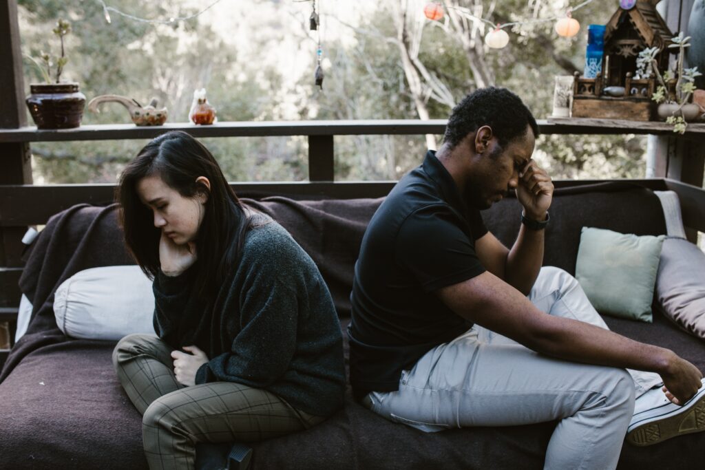 A couple sitting back-to-back on a bed in front of a window. Learn how couples therapists in Los Angeles and New York can help improve relationships today.