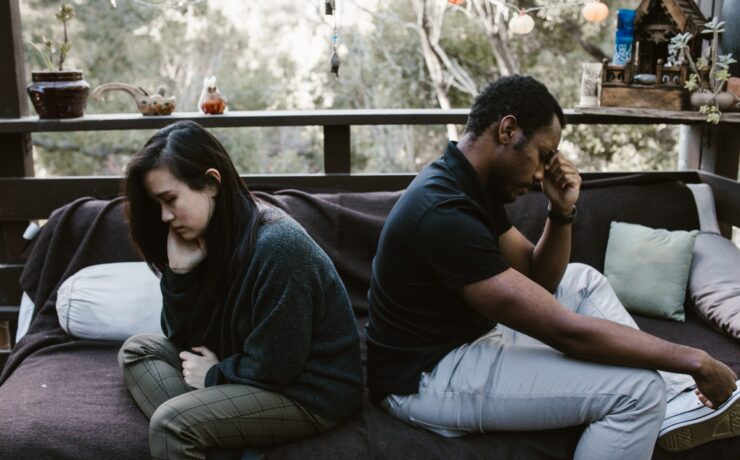 A couple sitting back-to-back on a bed in front of a window. Learn how couples therapists in Los Angeles and New York can help improve relationships today.