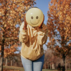 A person holds a balloon with a smiley face in front of their face. this could represent emotional masking that an Asian American therapist in Los Angeles, CA can help you address. Learn more about the help an Asian therapist in New York can offer by searching for an empath therapist in Los Angeles, CA today.
