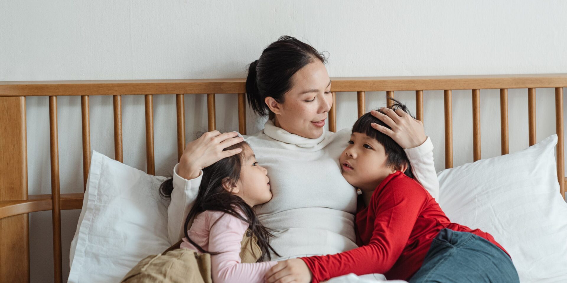 An Asian woman sitting in bed, holding two young children. Learn how an Asian American therapist in Los Angeles, CA can offer therapy for parenthood in Los Angeles, CA and other services. Search for Asian American pregnancy and postpartum therapy to learn more.