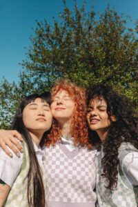 Three friends smile while embracing with arms around each other. This could represent the support therapy for teens in Los Angeles, CA can offer. Learn more about therapy for hsp in los angeles, CA, and other services. 

