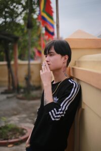 An Asian American smokes a cigarette while standing against a wall. This could represent the stress of trauma that an Asian American therapist in Los Angeles can address. Learn more about racial trauma in Los Angeles, CA or search for Asian American therapy in New York for more info today.
