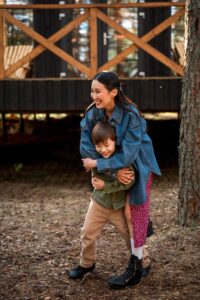 An Asian American mother smiles while hugging her happy child. This could represent the bonds created after working with an Asian American therapist in Los Angeles. Receive support via trauma therapy in Los Angeles, CA, and other services to overcome racial trauma in Los Angeles, CA today. 
