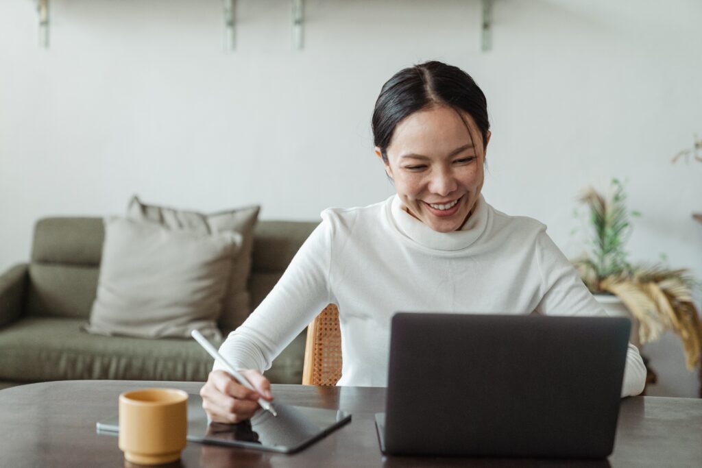 An Asian American woman sitting at a table, looking at a laptop, and taking notes. Learn workshops for Asian American in Los Angeles, CA can support your mental health. Contact an Asian American therapist in Los Angeles, CA or Asian therapist in New York for support.