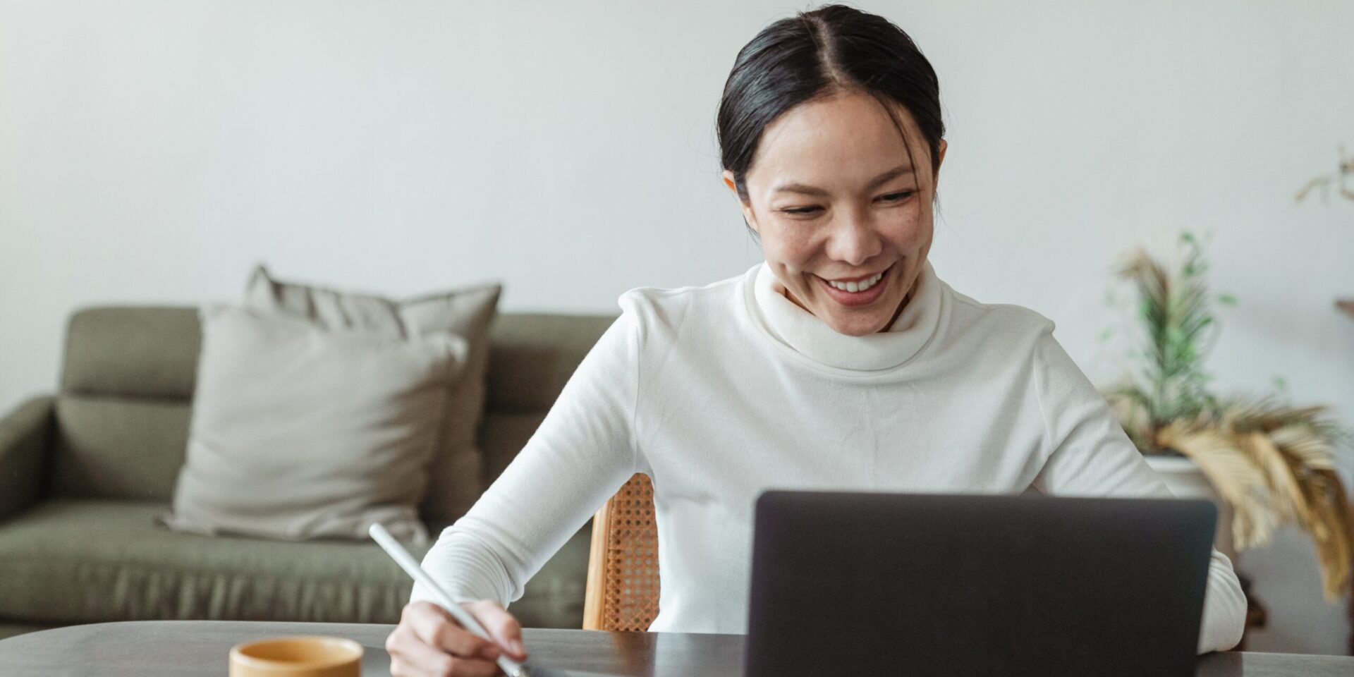 An Asian American woman sitting at a table, looking at a laptop, and taking notes. Learn workshops for Asian American in Los Angeles, CA can support your mental health. Contact an Asian American therapist in Los Angeles, CA or Asian therapist in New York for support.
