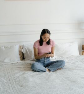 An asian american teen types on their phone while sitting on a bed. Learn how an Asian therapist in New York can help your teen and their mental health concerns. Contact an Asian American therapist or search for online therapy for teens in California for support today.
