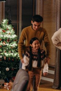 An adult walks with their smiling child in front of a christmas tree. Learn how an Asian therapist in Los Angeles, CA can offer support with Asian American therapy near me. Search for Asian American therapy near me today. 
