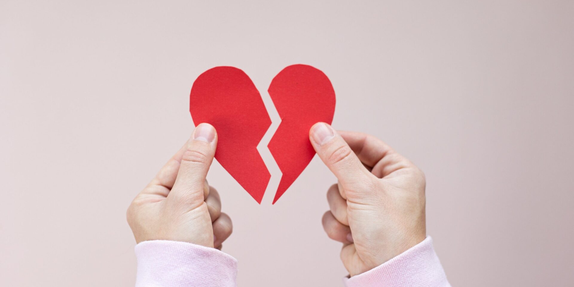 Two hands holding two sides of a paper heart broken in half. This could represent the heartbreak that individual therapy in LA and New York can address. Learn about trauma therapy near me and more today.
