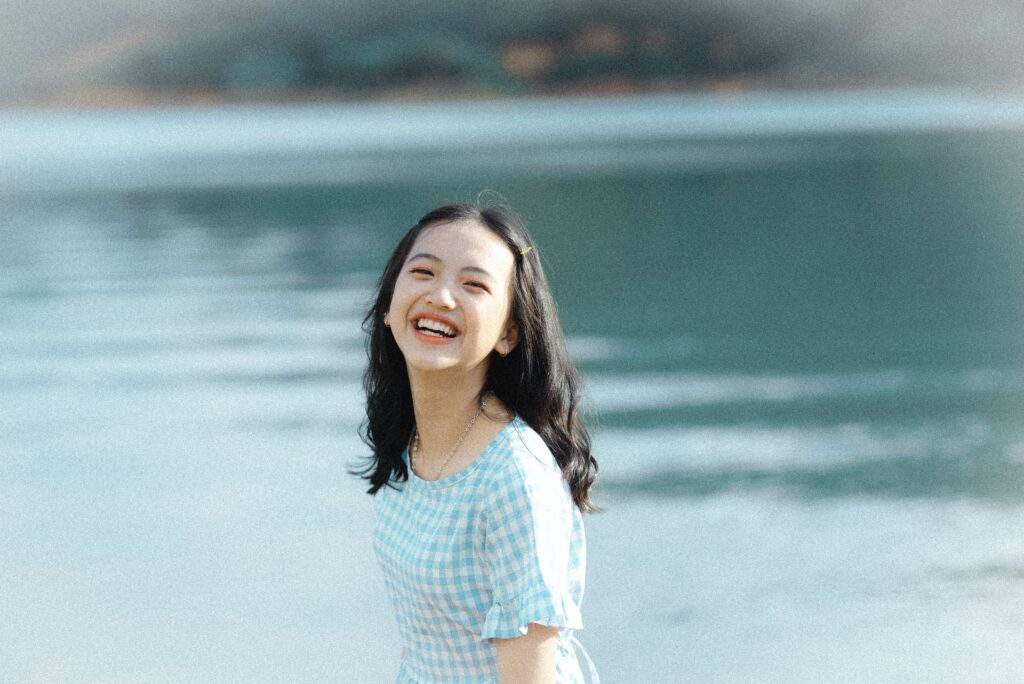 A teen smiles at the camera while standing in front of a lake. Learn how therapy for teens in Los Angeles, CA can help your teen become independent. Search for online therapy for teens in California to learn more about Asian American therapy in New York today.