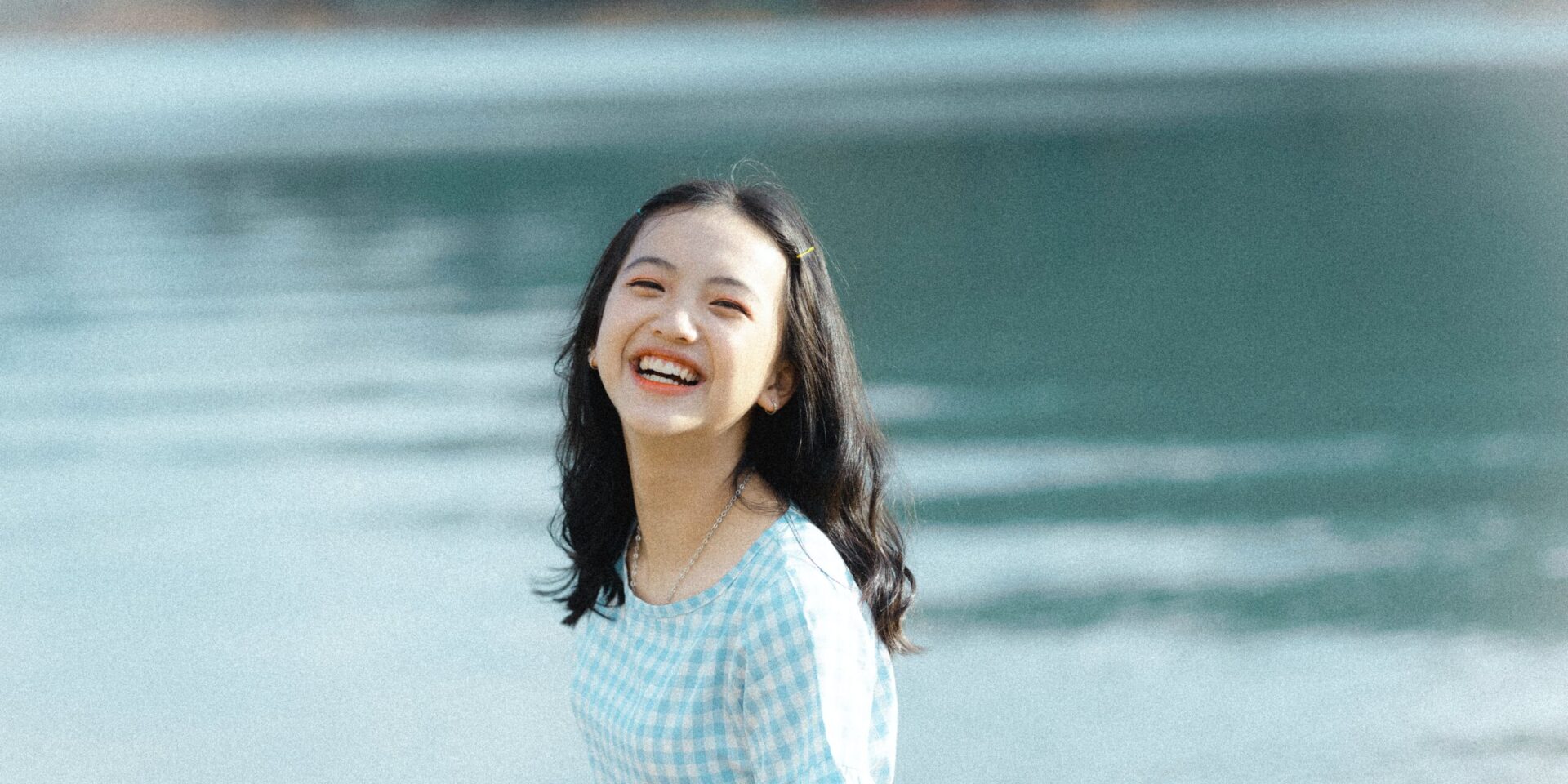 A teen smiles at the camera while standing in front of a lake. Learn how therapy for teens in Los Angeles, CA can help your teen become independent. Search for online therapy for teens in California to learn more about Asian American therapy in New York today.