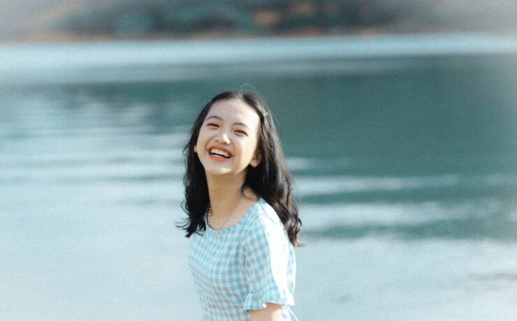 A teen smiles at the camera while standing in front of a lake. Learn how therapy for teens in Los Angeles, CA can help your teen become independent. Search for online therapy for teens in California to learn more about Asian American therapy in New York today.