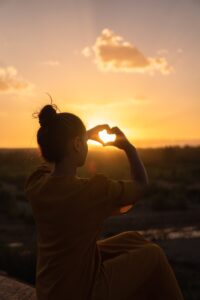 A person holds up their hands toward a sunset in the shape of a heart. This could represent recovering from heartbreak after individual therapy in Los Angeles, CA. Search for online trauma therapy in california by contacting an Asian American therapist today.
