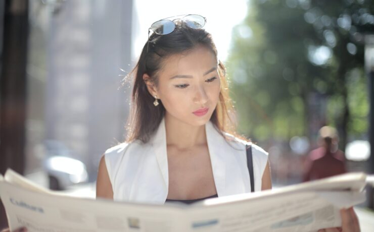 A woman reads the newspaper on a sunny day. Search how Asian American therapy can offer support with addressing traumatic news. Contact an Asian American therapist in California for more support.
