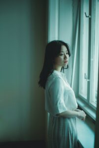 An Asian American woman looks out a window with a somber expression. Learn how an Asian American therapist in Los Angeles can offer support by searching for therapy for Asian women in Los Angeles, CA and beyond. Search for Asian American therapy in New York today.
