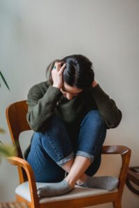 A woman sits in a chair with hands against their ears while bowing their head. This could represent the stress of anxiety that an Asian American therapist can offer support with. Search for an Asian American therapist near me or online anxiety treatment in California. Or, search for anxiety treatment in Los Angeles, CA today.
