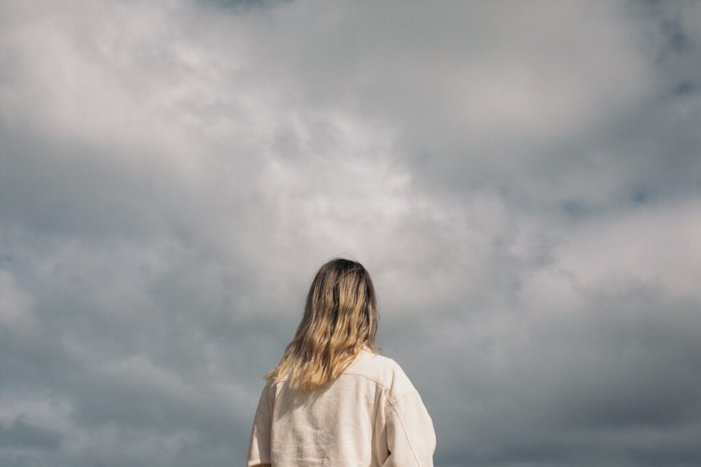 A woman facing away from the camera looks up at a cloudy sky. This could represent the effects of seasonal affective disorder that individual therapy in Los Angeles, CA. Learn more about the benefits of having a therapist that is culturally sensitive in Los Angeles, CA. Search for online therapy in California to learn more.